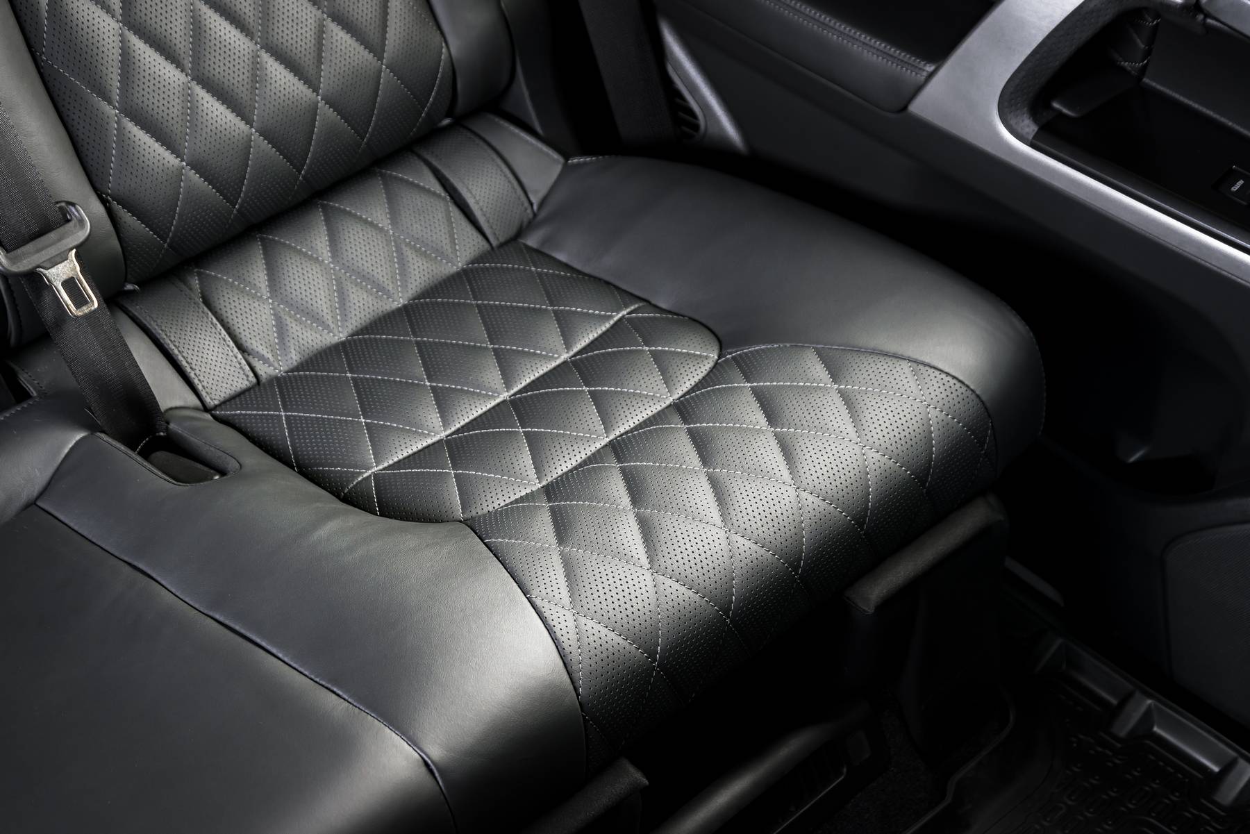 Back passenger seats in modern luxury car, frontal view, black perforated leather with stitching
